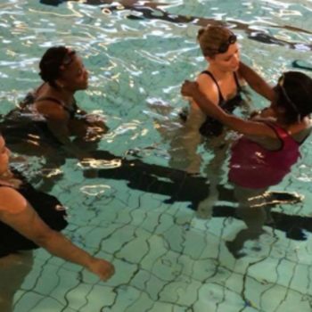 Fire kvinner i et basseng øver på å flyte på ryggen