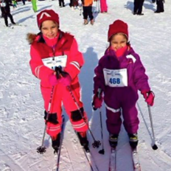 To blide jenter ca 6-8 år på ski med nummerlapp foran på parkdressene