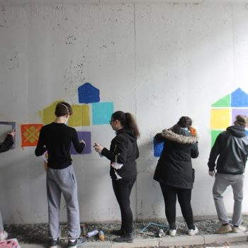 Ungdommer maler fargerike mønstre på en grå murvegg i en fotgjengerundergang.