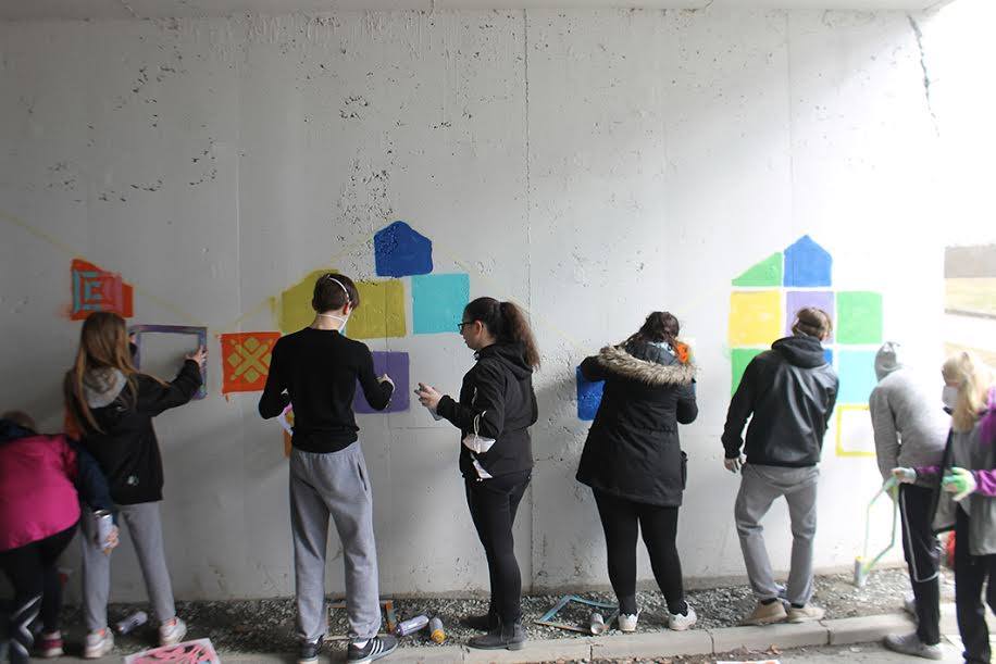 Ungdommer maler fargerike mønstre på en grå murvegg i en fotgjengerundergang.